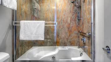 Un baño con bañera de hidromasaje con mampara de vidrio, pared de mármol y perchero.