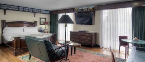 A hotel room with a bed, a desk, a chair, a dresser, a lamp, and a TV.