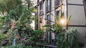 Ein friedlicher Garten mit Teich, üppigem Grün und einem Gebäude mit großen Fenstern und Balkonen.