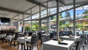 Un restaurante con mesas dentro, amplias ventanas y vistas a una piscina al aire libre.