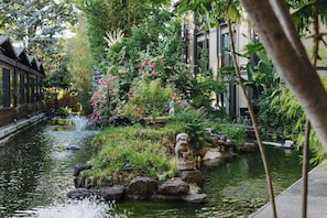 A serene garden with a pond, lush greenery, and a traditional stone lion statue.