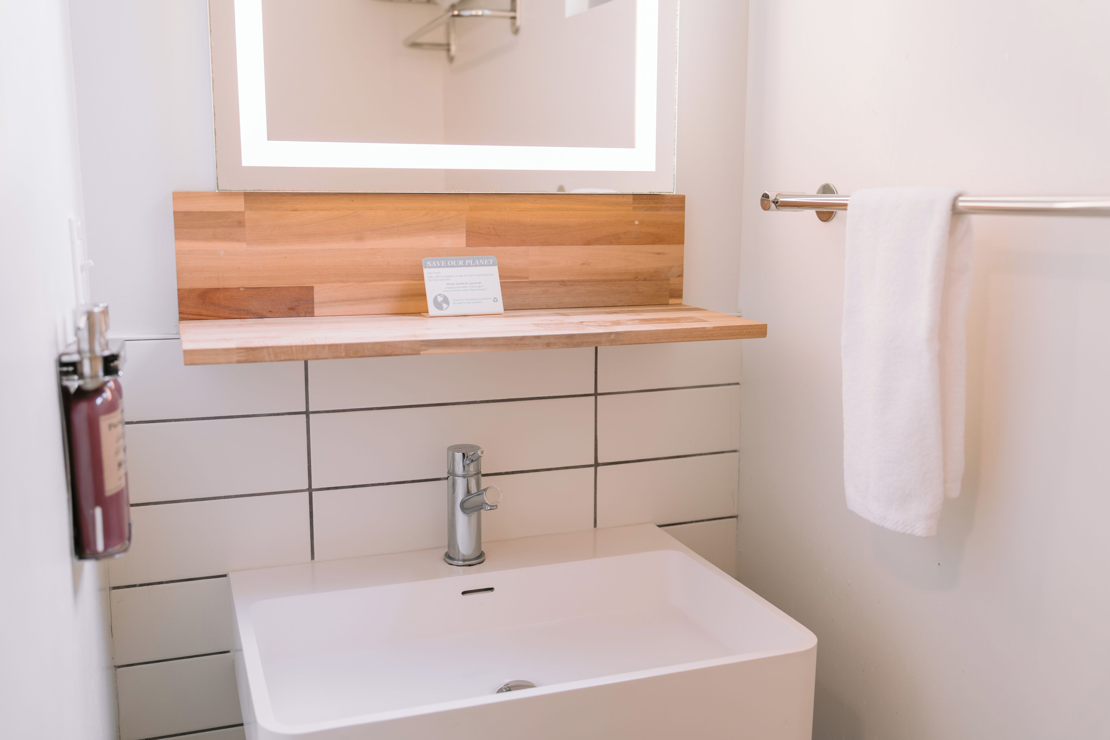 A bathroom with a white sink, a wooden shelf above it, and a towel rack to the right.