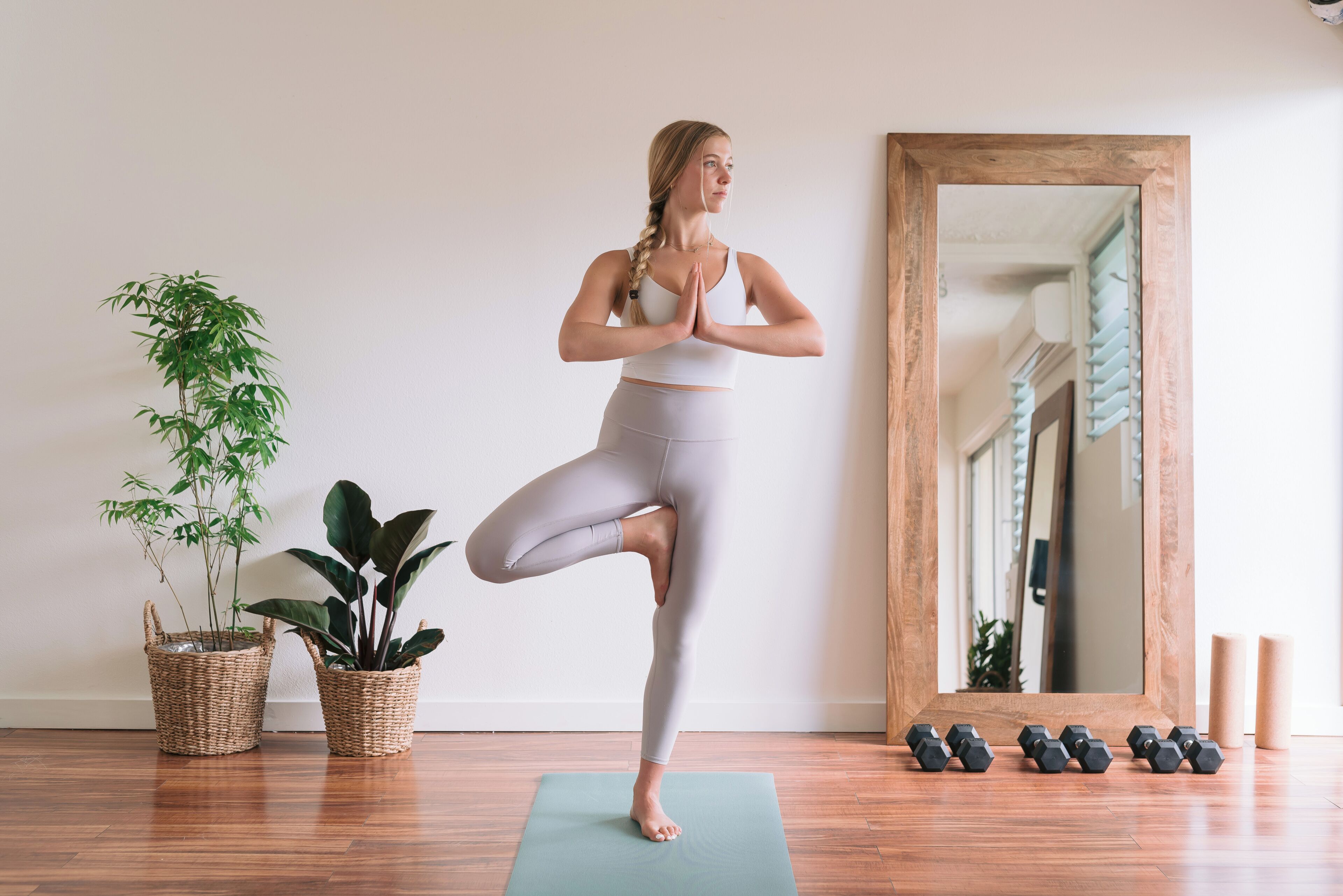 A person in a yoga pose on a mat, with a mirror and dumbbells on the floor.