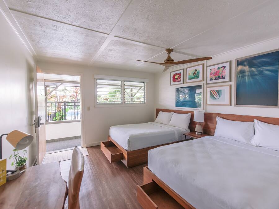 Quarto com duas camas, uma escrivaninha de madeira, um ventilador de teto e obras de arte nas paredes.
