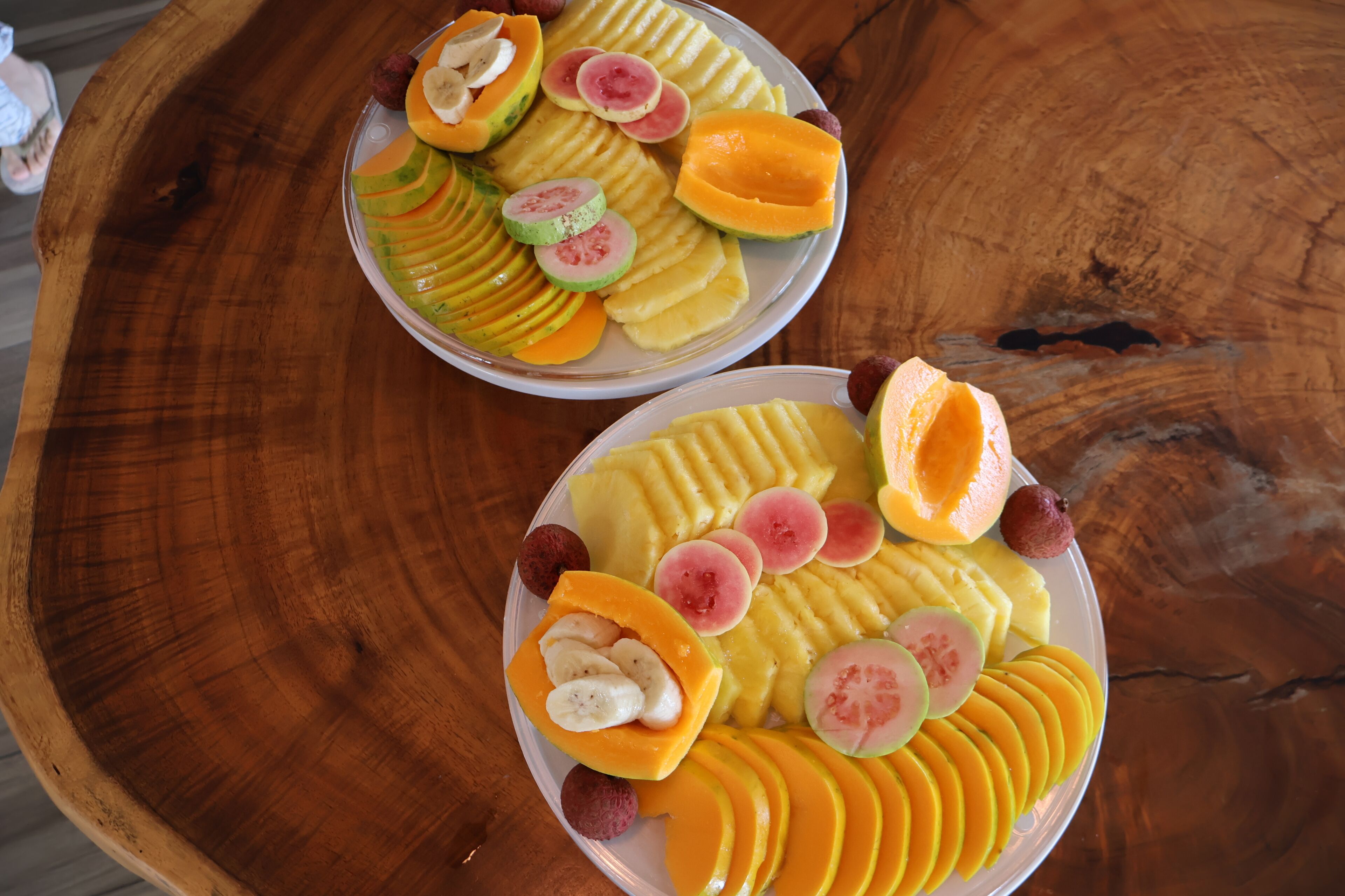 Two plates of sliced fruits on a wooden table.