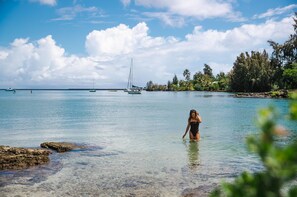 A woman in a swimsuit standing in shallow water near a beach with boats and palm trees in the background. - SCP Hilo Hotel (Hilo)