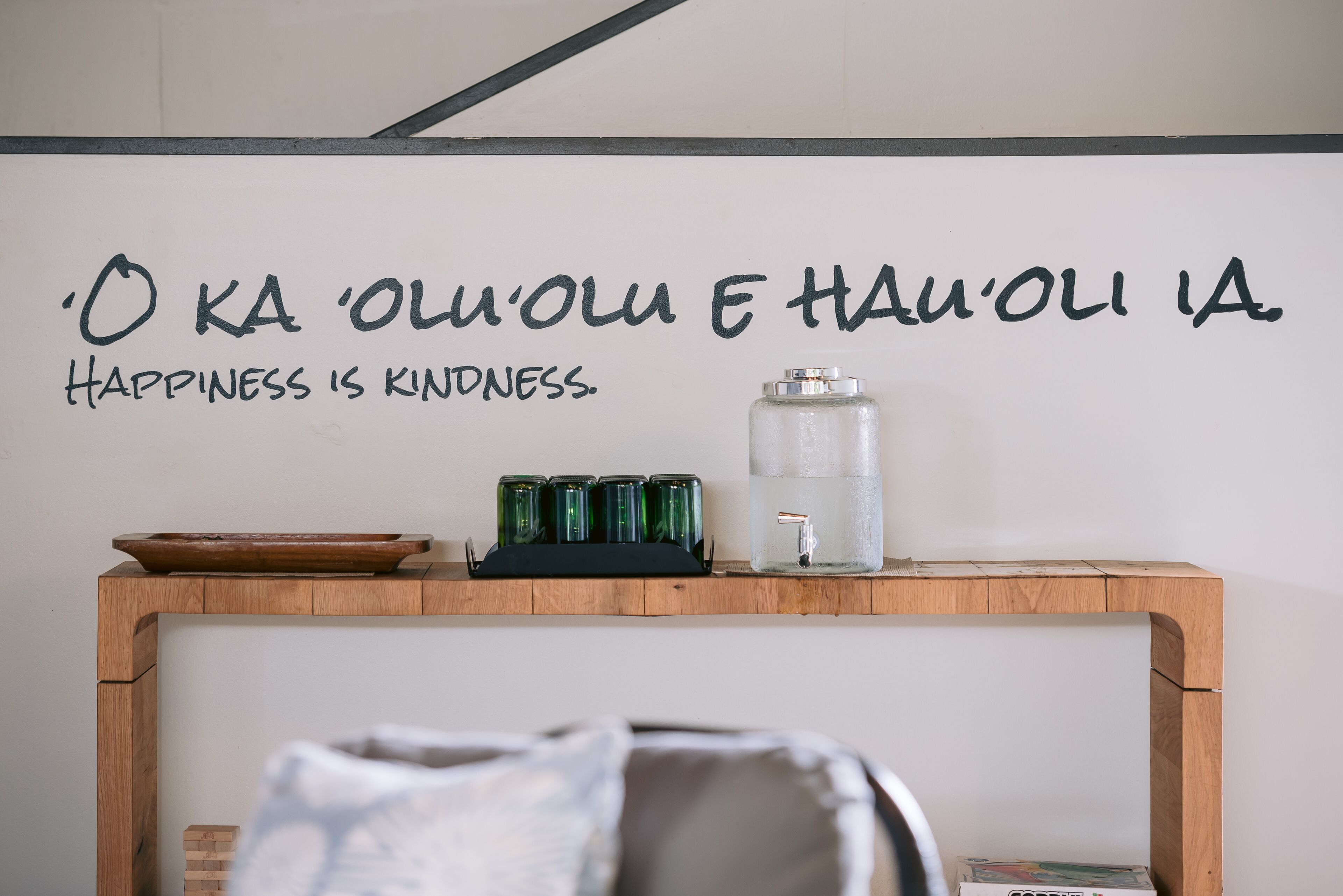 A wall with a quote in a foreign language and a wooden table with a water dispenser and glasses.