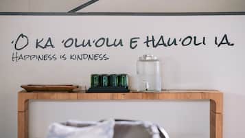 A wall with a quote in a foreign language and a wooden table with a water dispenser and glasses.