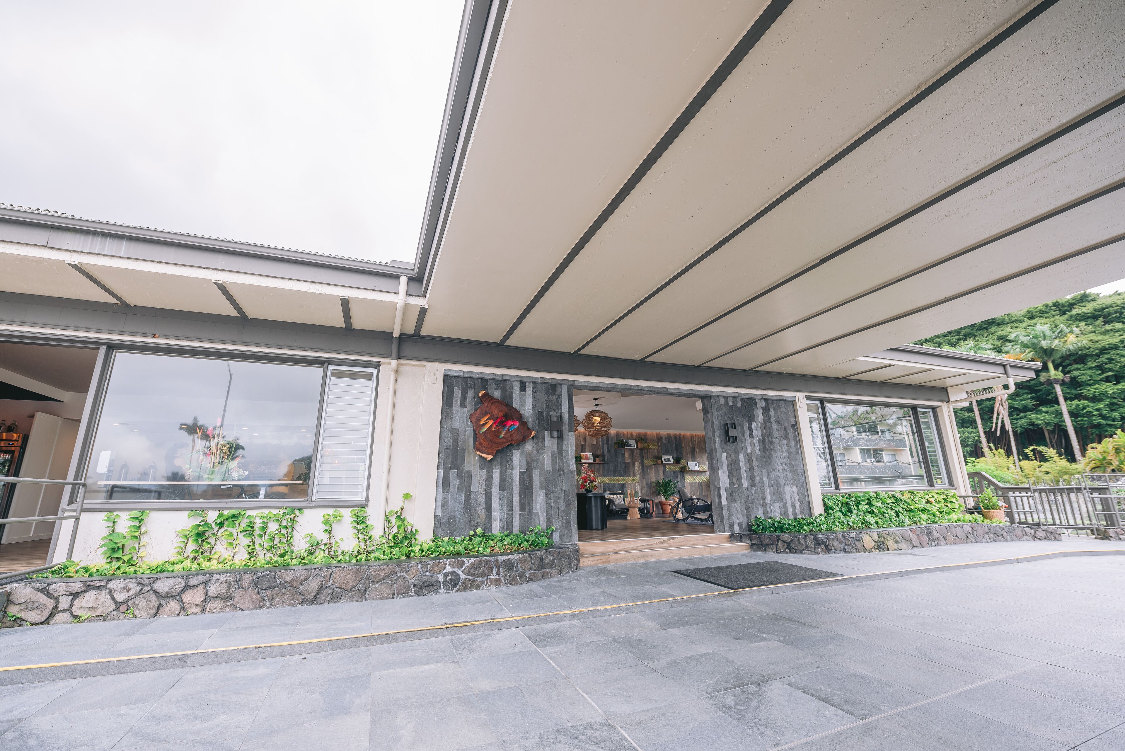 A modern building with a covered entrance, large windows, and a stone planter with greenery.