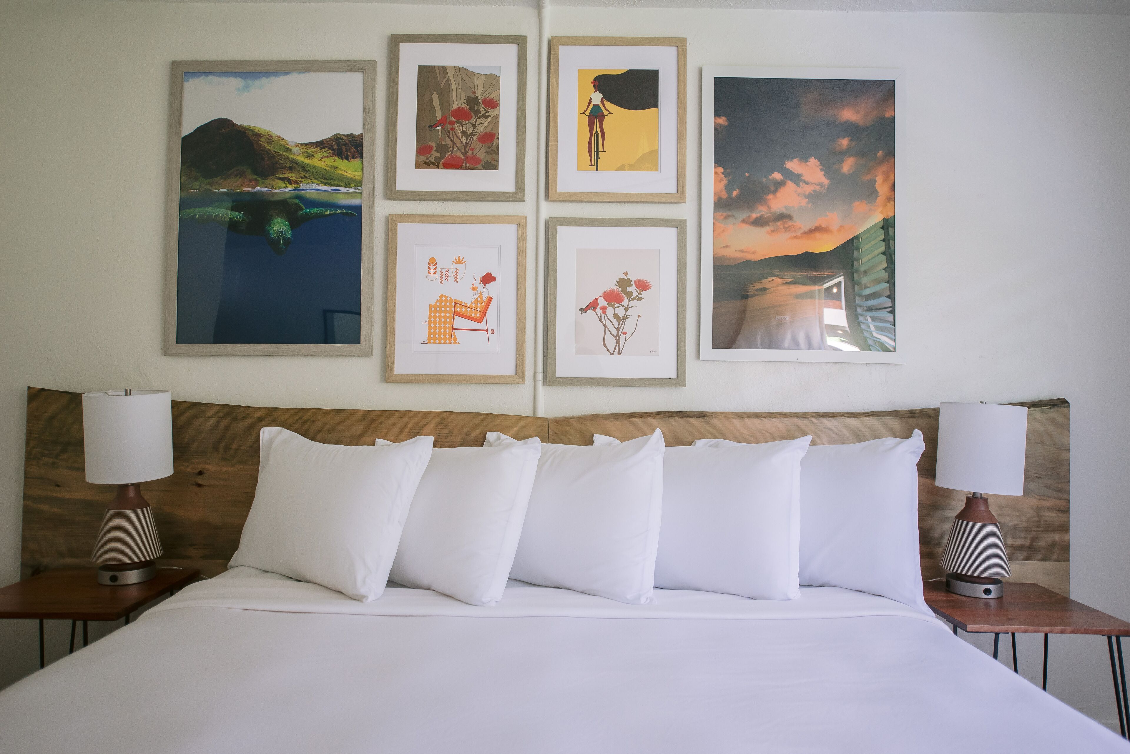 Una habitación de hotel con una cama grande, ropa de cama blanca, dos mesitas de noche con lámparas y cuatro cuadros enmarcados en la pared.