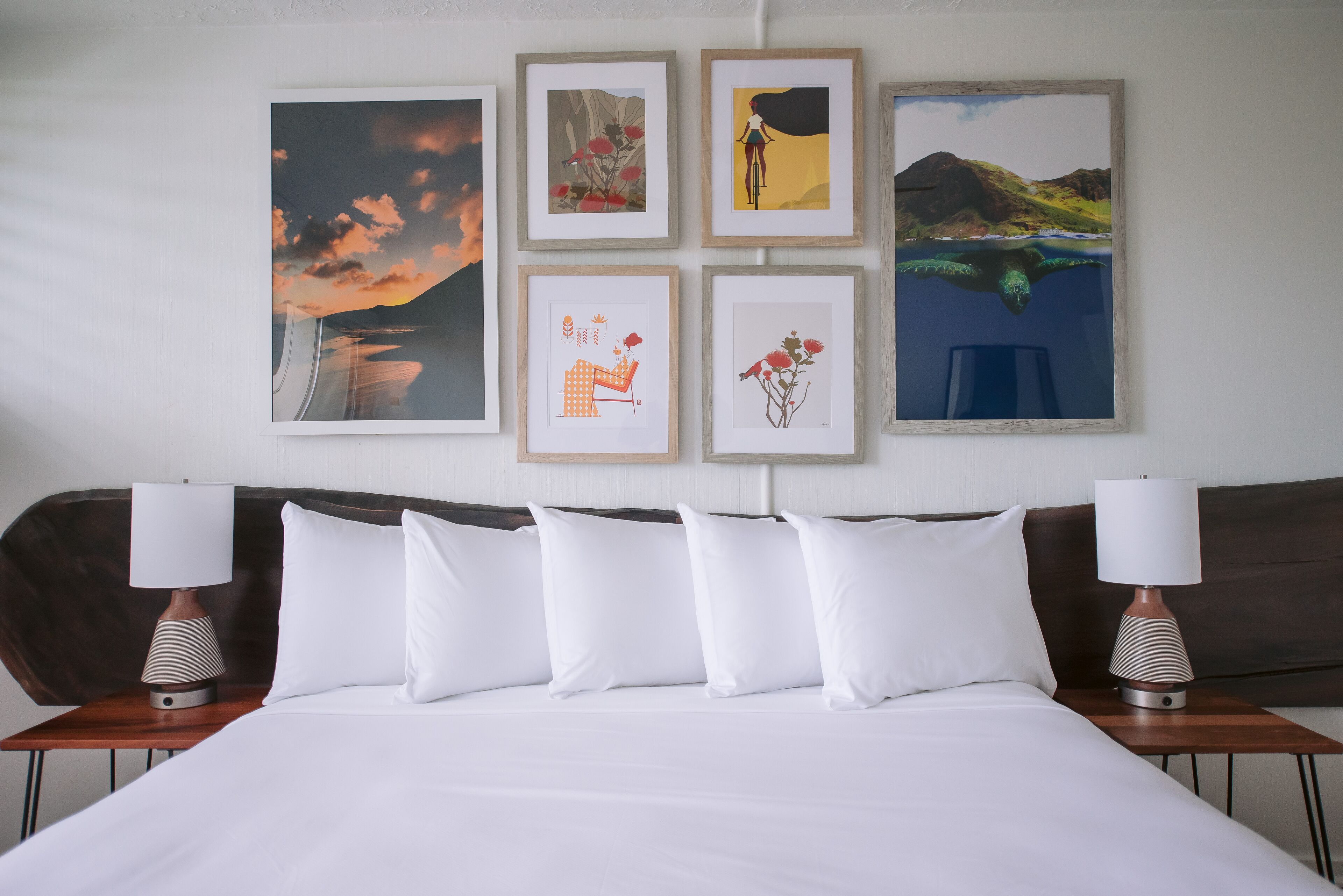 A hotel room with a large bed, white bedding, and a headboard. There are framed artworks on the wall above the bed.