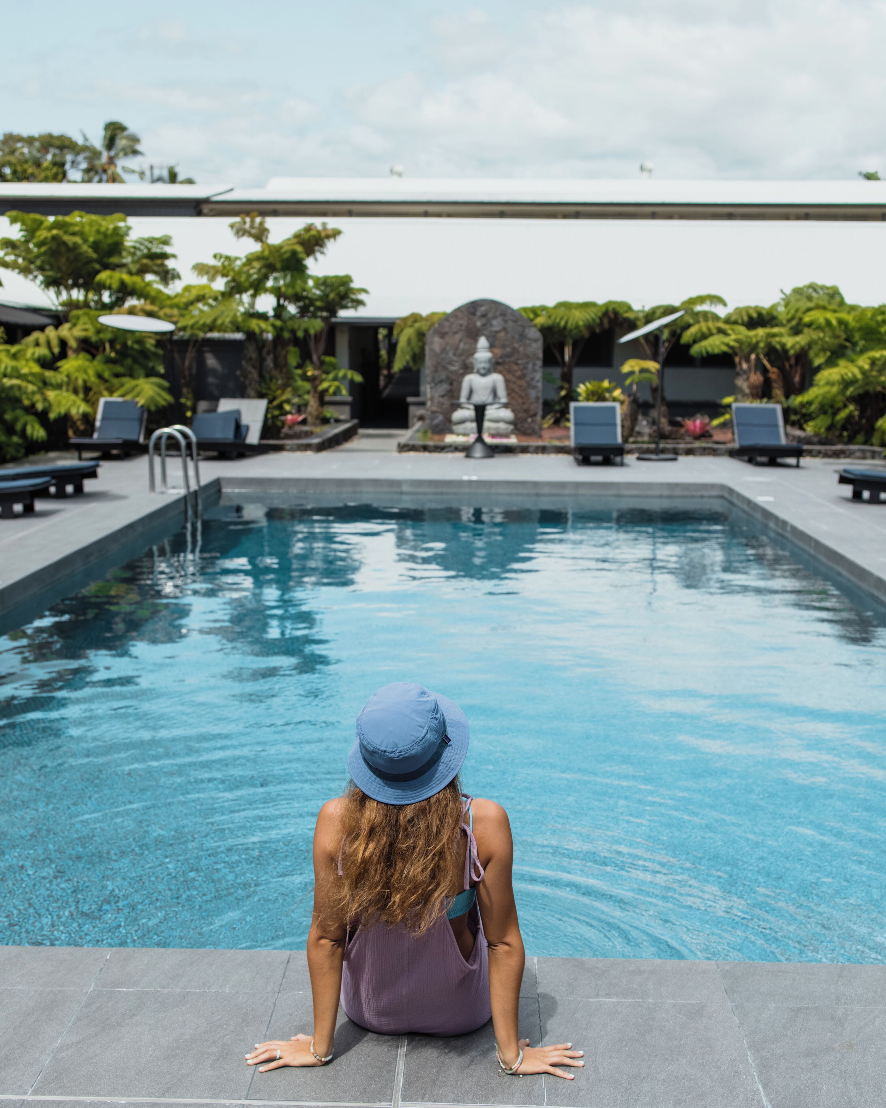 A woman sitting by a pool with a Buddha statue in the background.