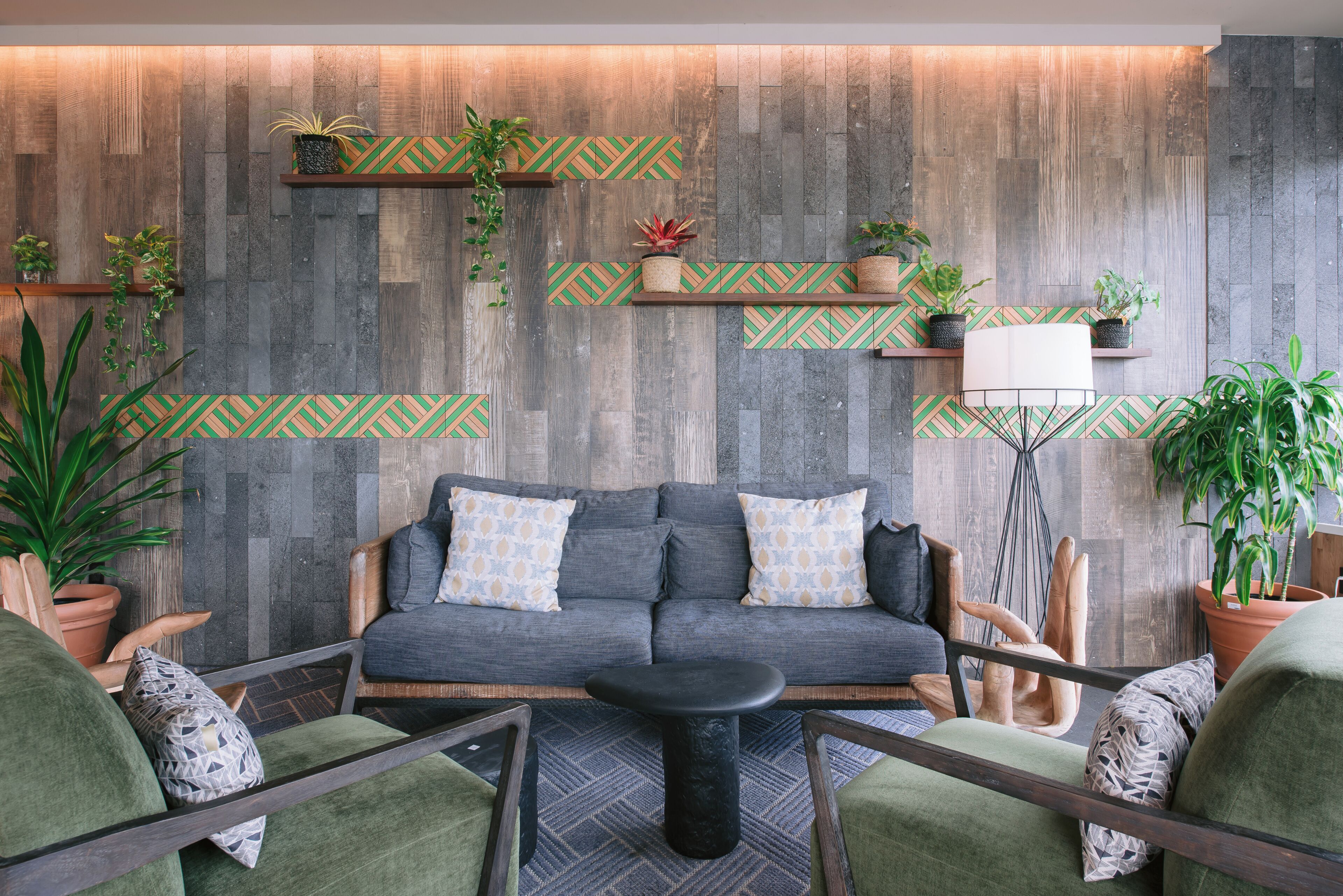 Una sala de estar moderna con un sofá gris, sillones verdes, una mesa de centro negra y estanterías de madera con plantas.