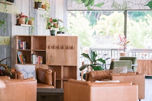 A cozy living area with a wooden bookshelf, leather sofas, and a large window offering a view of greenery.