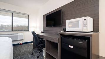Ett hotellrum med en säng, ett skrivbord med en mikrovågsugn, en tv och ett kylskåp.