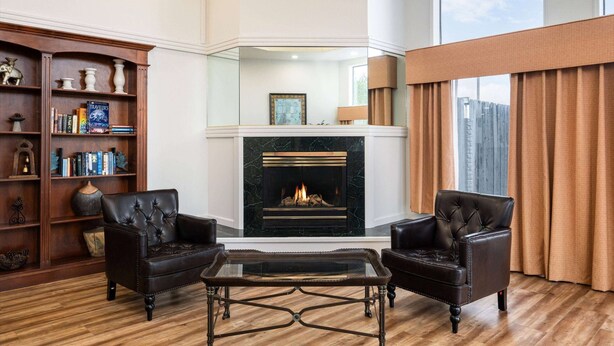 A living room with a fireplace, leather armchairs, a glass coffee table, and a wooden bookshelf. - Baymont by Wyndham Bellingham (Bellingham)