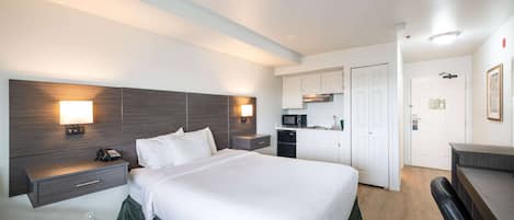 Una habitación de hotel con una cama grande, mesitas de noche, un escritorio, un microondas y un rincón americano.