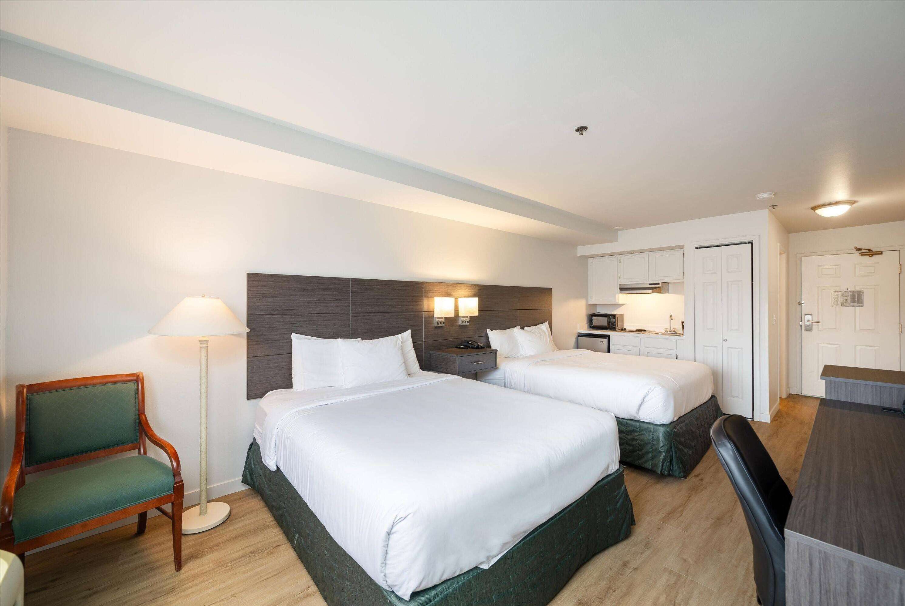 A hotel room with two beds, a desk, a chair, a lamp, and a wardrobe.