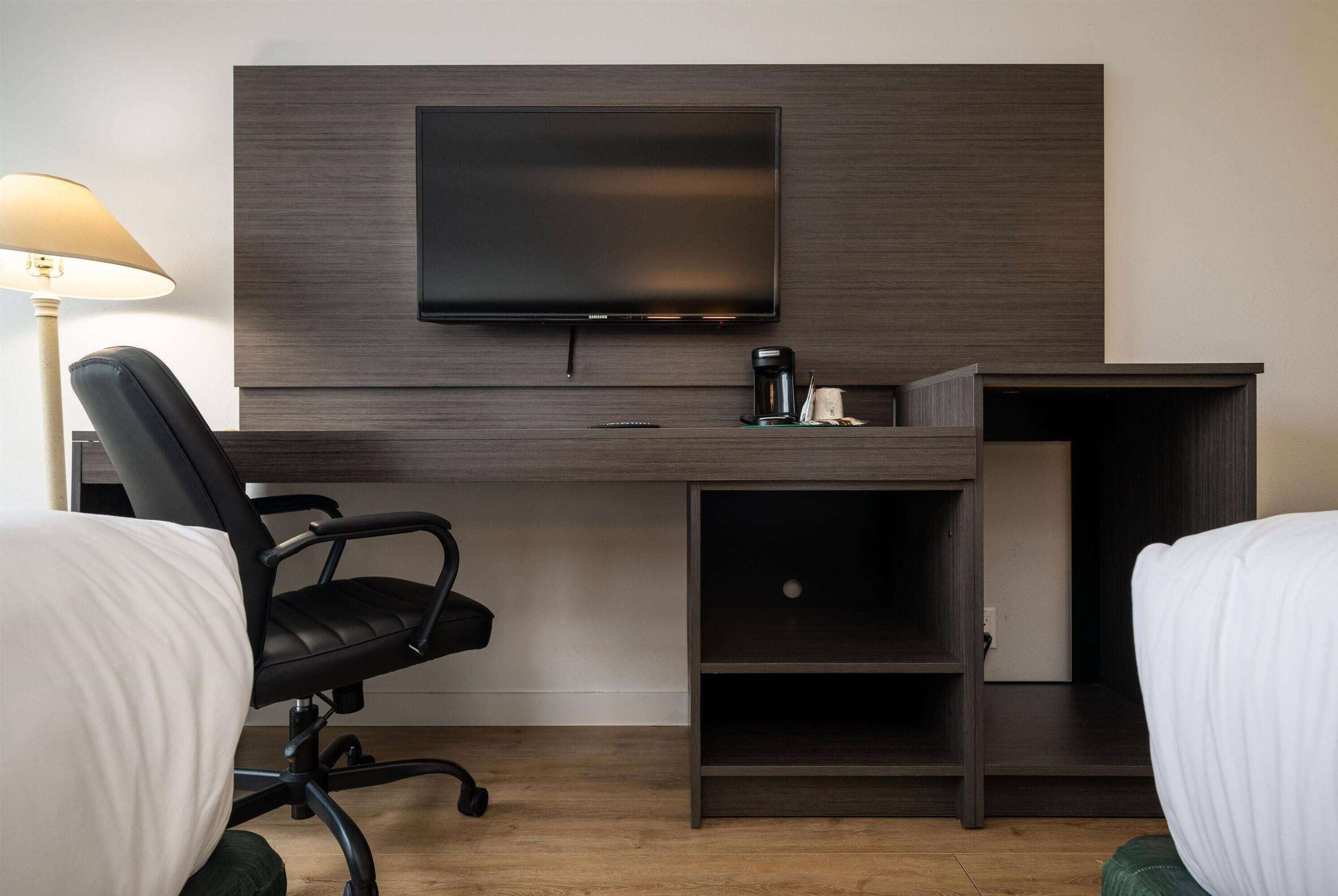 A hotel room with a bed, a desk with a TV, a chair, and a coffee maker.