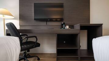 Habitación de hotel con cama, escritorio con televisor, una silla y cafetera.