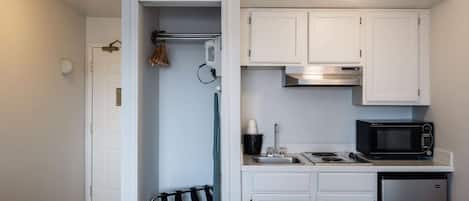 A compact kitchen with white cabinets, a microwave, a sink, and a small refrigerator.