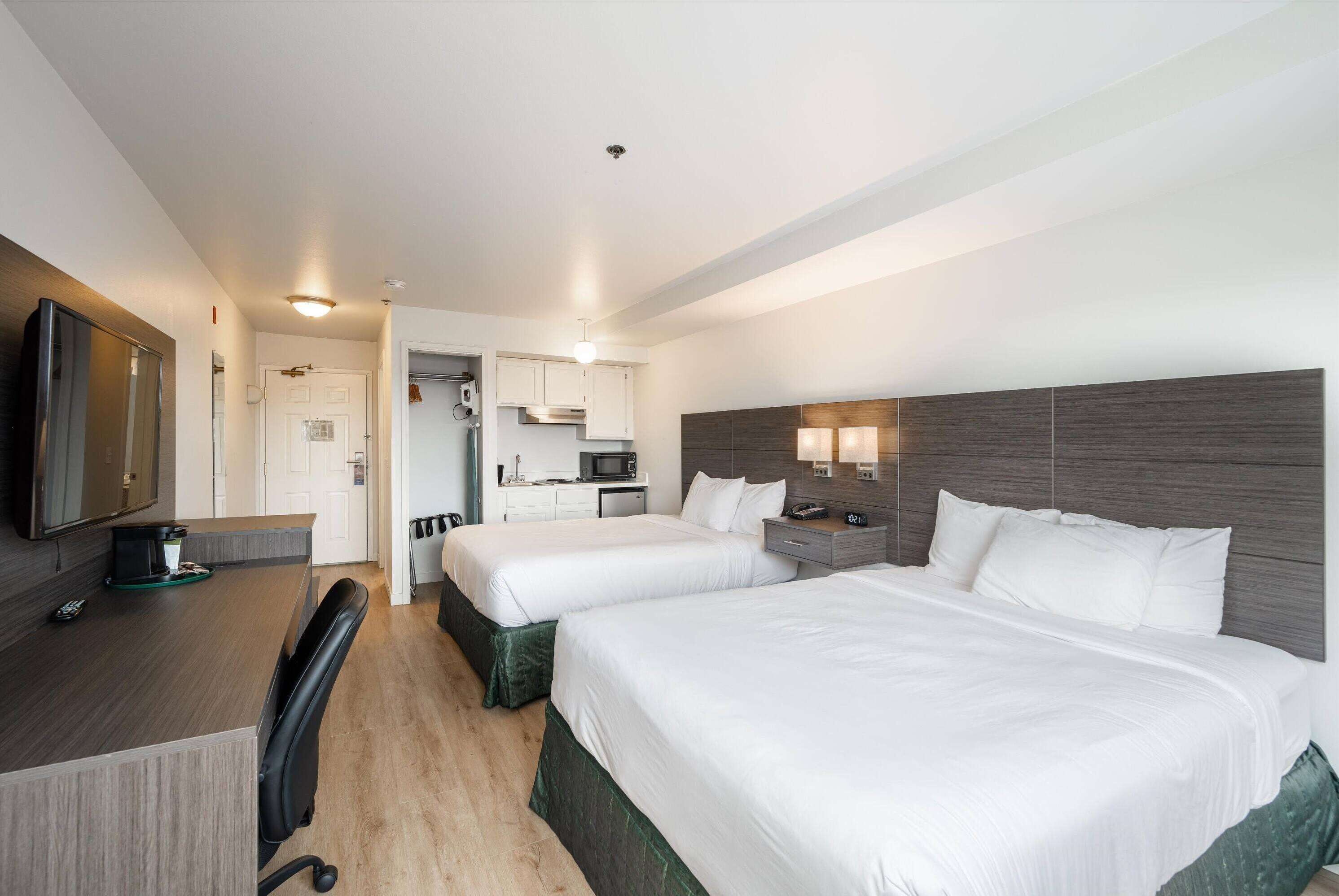 A hotel room with two beds, a desk with a computer, a microwave, and a TV.