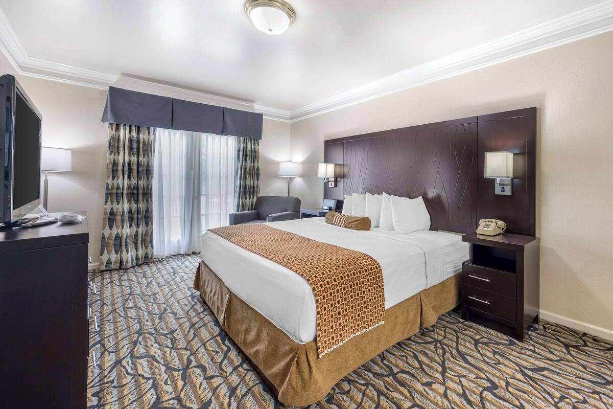 A hotel room with a large bed, a desk, a chair, a TV, and a telephone.