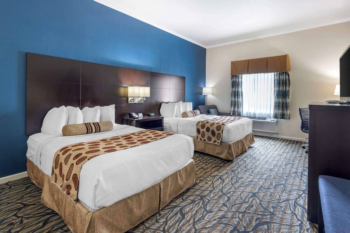 A hotel room with two beds, a desk, a chair, a large mirror, and a window with curtains.