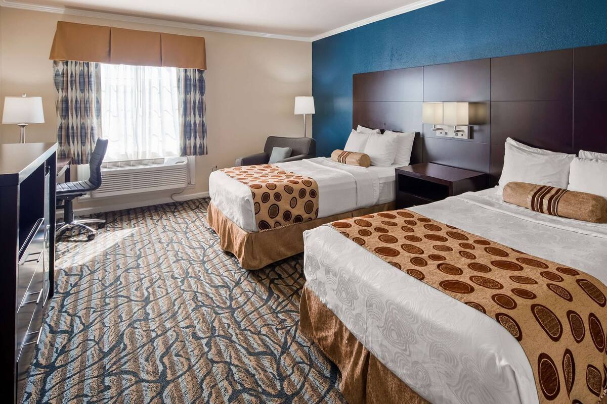 A hotel room with two beds, a desk, a chair, a lamp, and a patterned carpet.