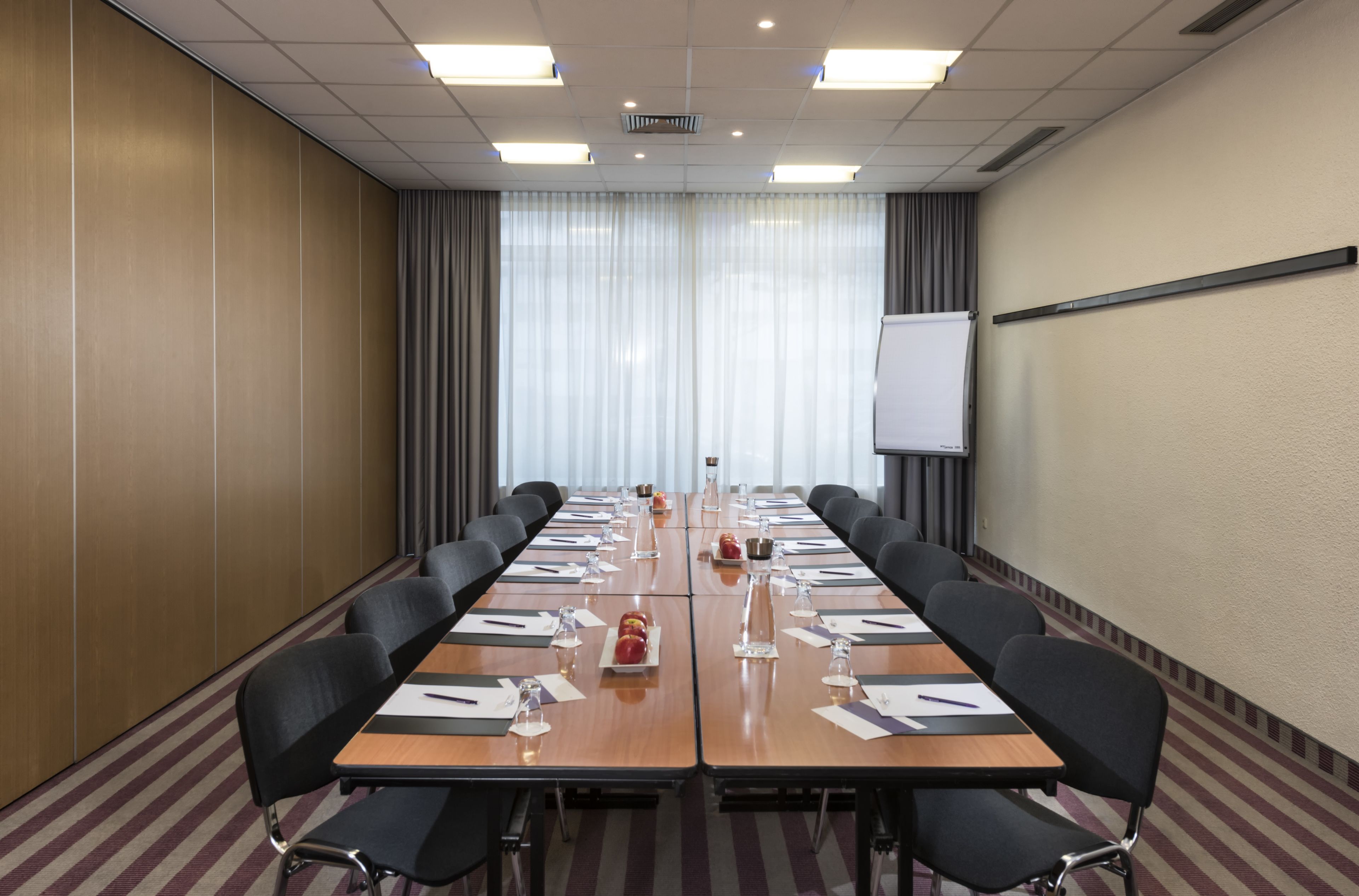 Ein Konferenzraum mit langem Tisch, Stühlen, einer Whiteboard und einer Projektionsleinwand.