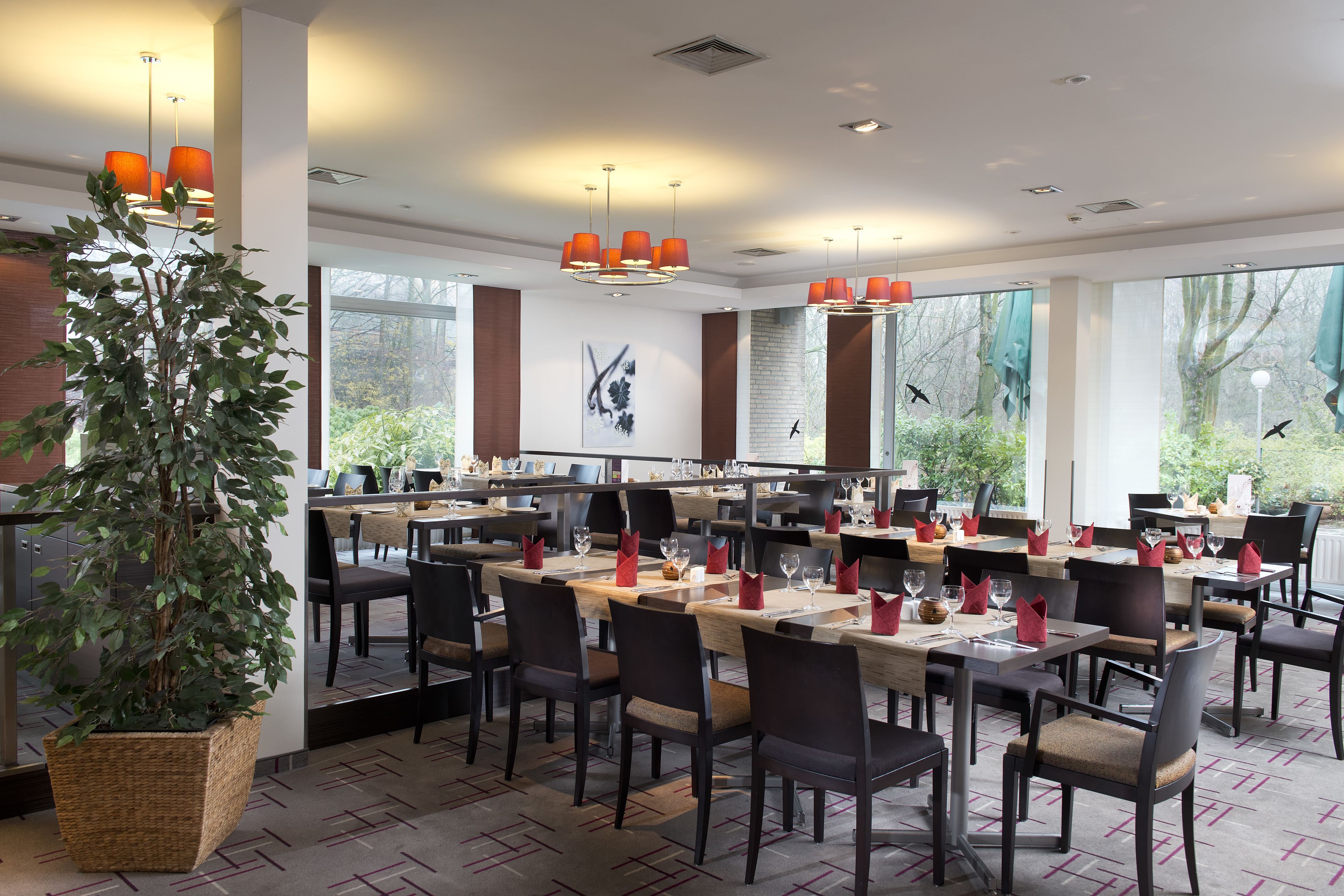 Ein Restaurant mit mehreren Tischen, Stühlen und einer großen Kübelpflanze.