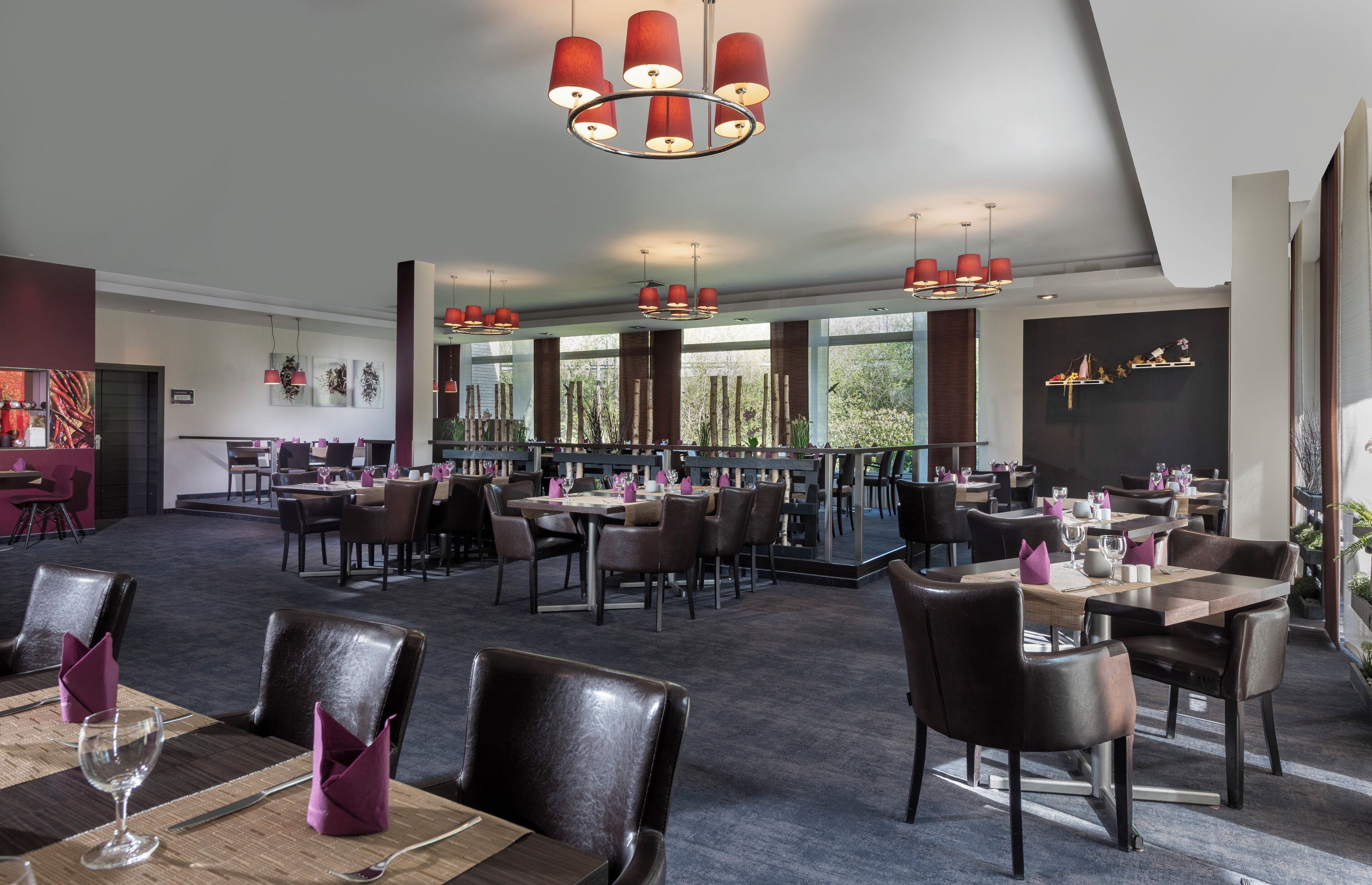 Un restaurante espacioso con techos altos, candelabros modernos y vistas al exterior.
