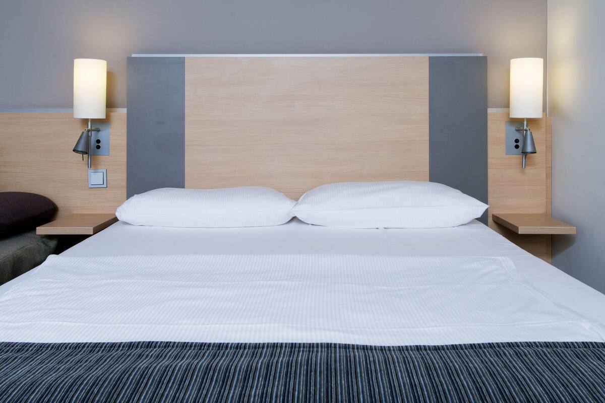 A hotel room with a large bed, two bedside tables, and wall-mounted lamps.