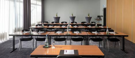 Une salle de conférence équipée de plusieurs tables, de chaises et de plantes en pot.