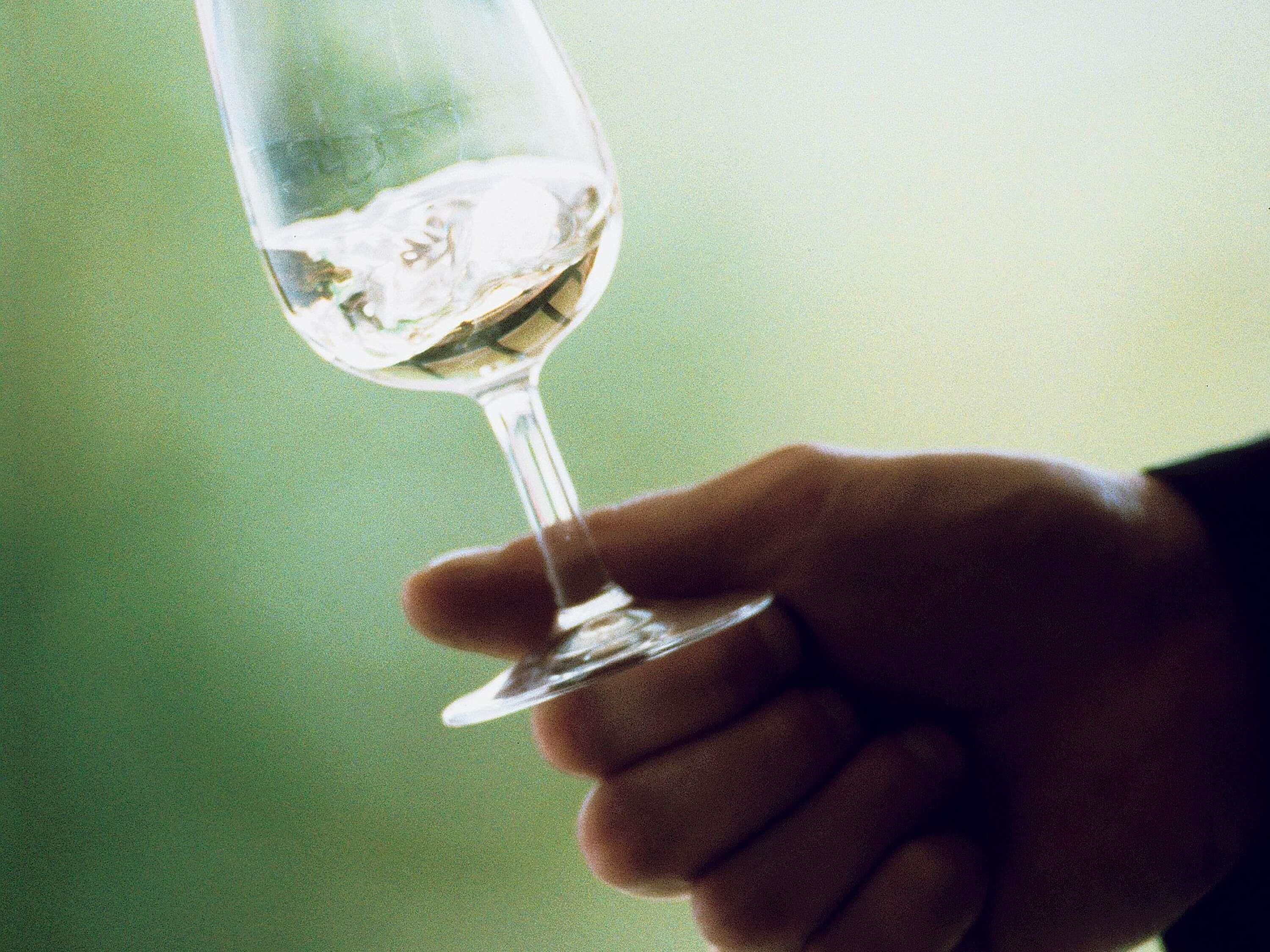 A hand holding a clear glass with a liquid, possibly a beverage, against a blurred background.