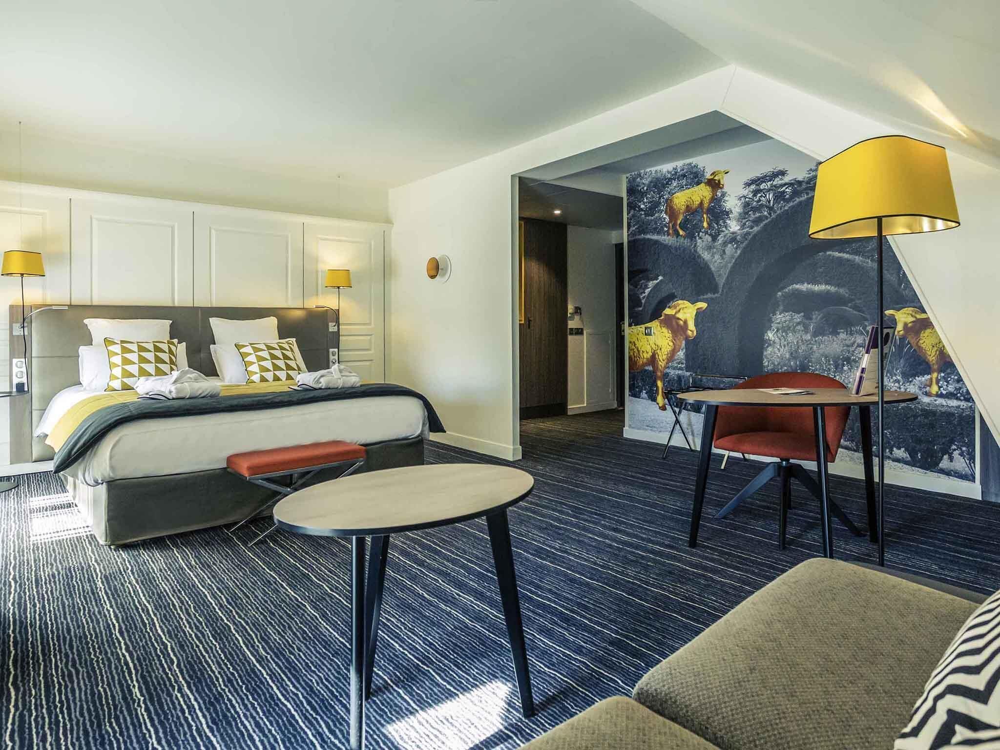 Una habitación de hotel con una cama, una mesita pequeña, una silla y un mural en la pared.