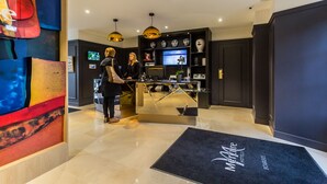 Zona de recepción con un mostrador moderno, una pantalla grande y una alfombra negra con el nombre del hotel.