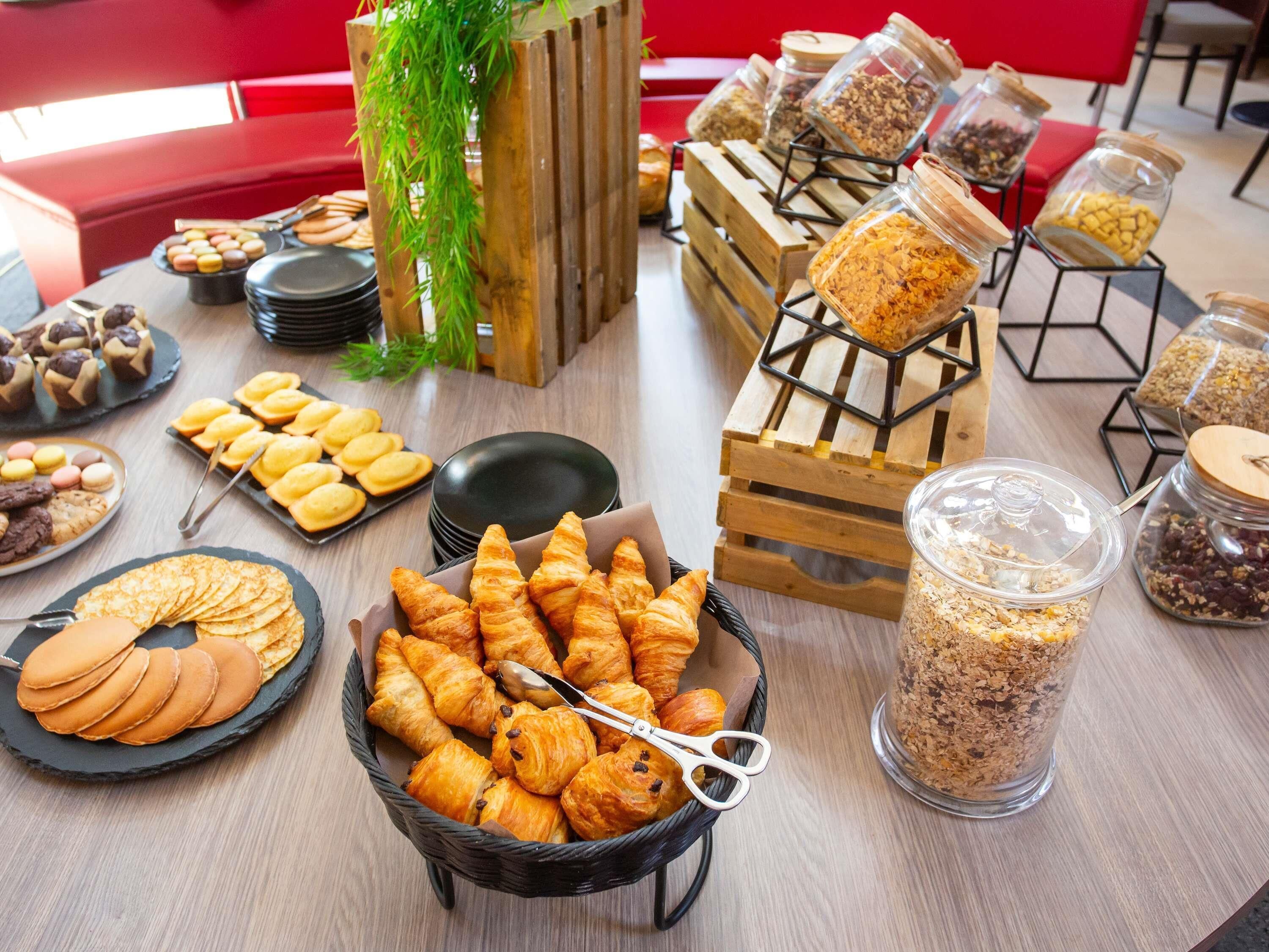 Een buffet tafel met diverse gebakjes, een mand croissants en potten granola.
