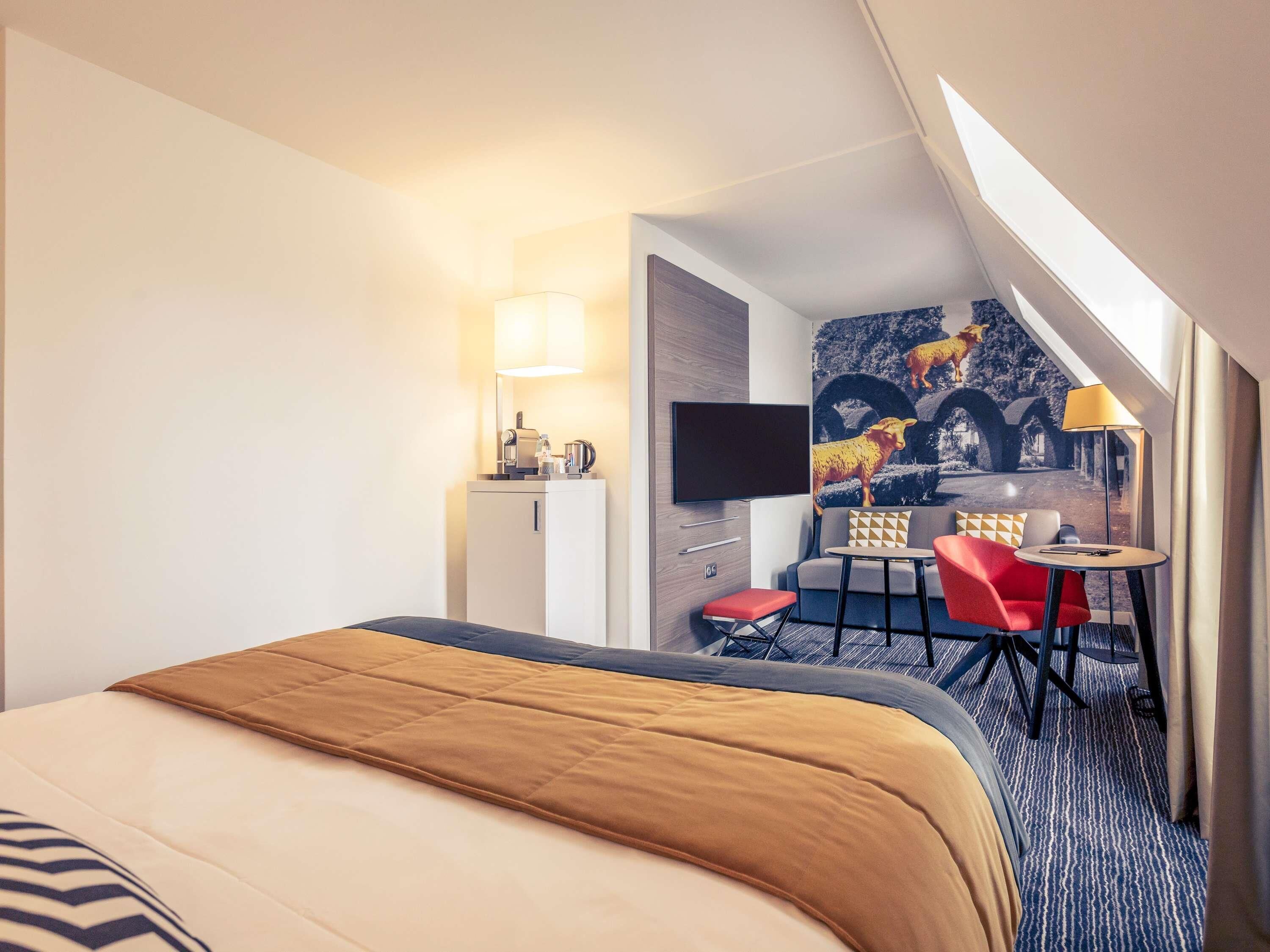 Un cuarto de hotel con cama, escritorio, silla, televisión y un cuadro en la pared.