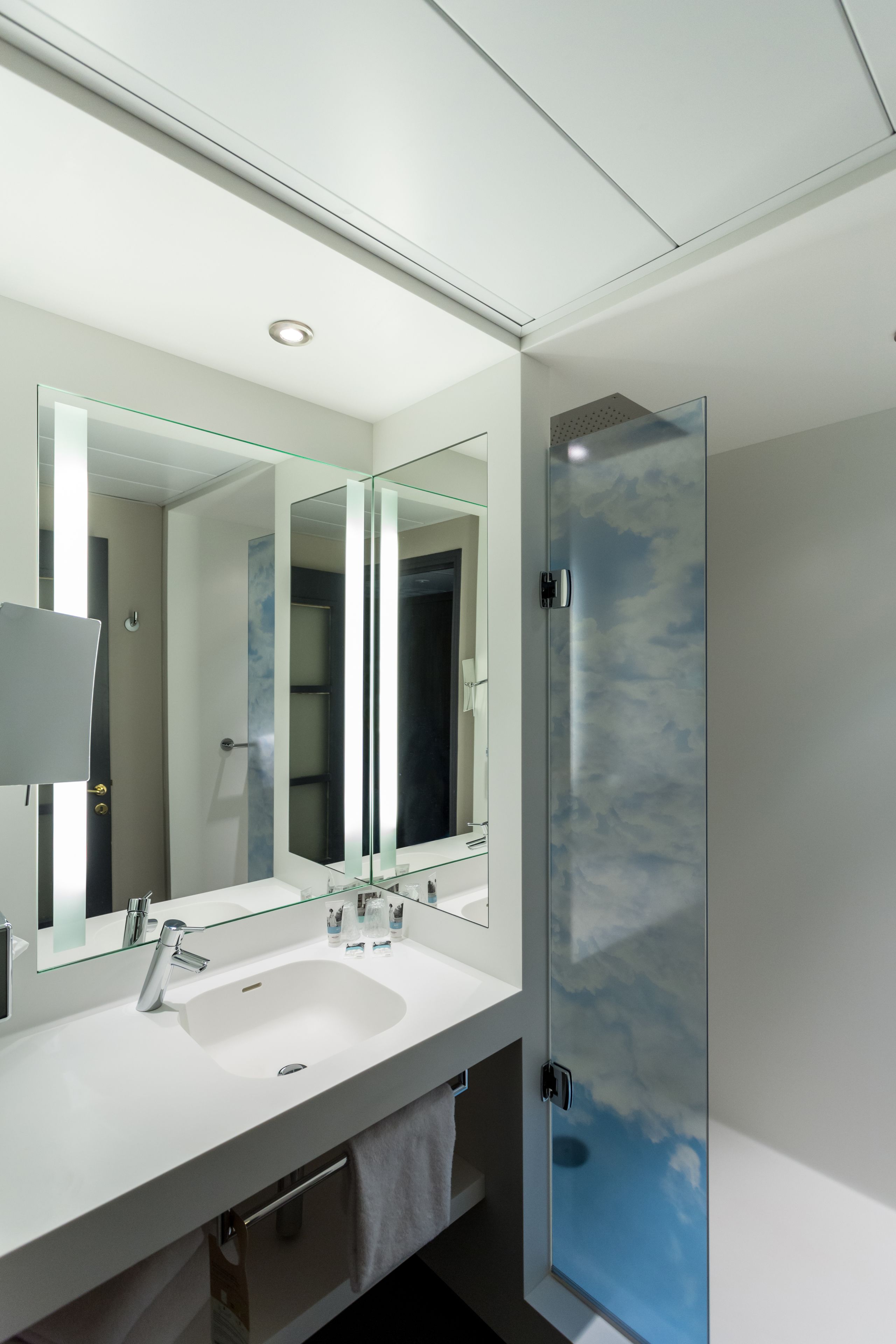 A modern bathroom with a large mirror, a white sink, and a glass shower enclosure.