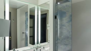 A modern bathroom with a large mirror, a white sink, and a glass shower enclosure.