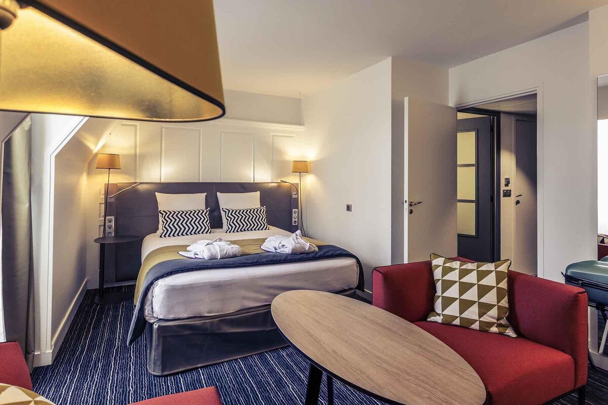 A hotel room with a bed, bedside tables, a desk, a chair, and a lamp.