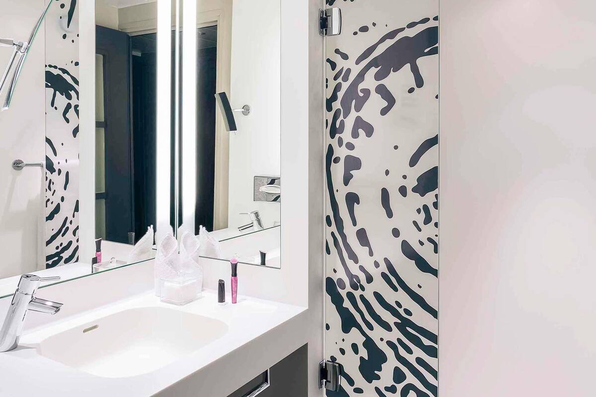 Ein modernes Badezimmer mit einem weißen Waschbecken, einem großen Spiegel und einer Tür mit einem schwarz-weißen abstrakten Muster.