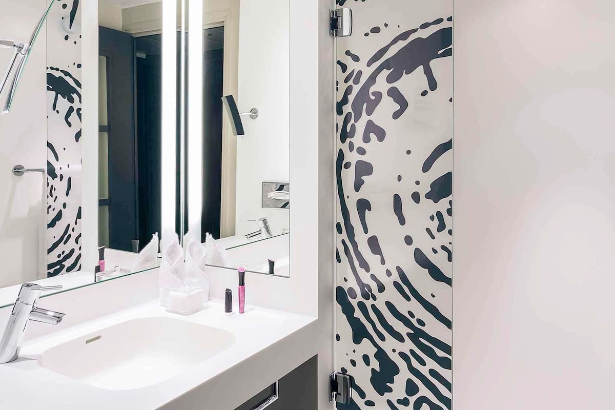 A modern bathroom with a white sink, a large mirror, and a door with a black and white abstract pattern.