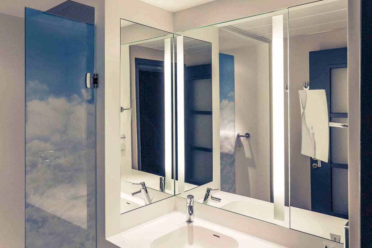 Une salle de bain moderne avec un grand miroir, un lavabo blanc et un espace douche.