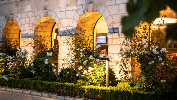 Un edificio de piedra con ventanas arqueadas y un jardín con flores blancas.