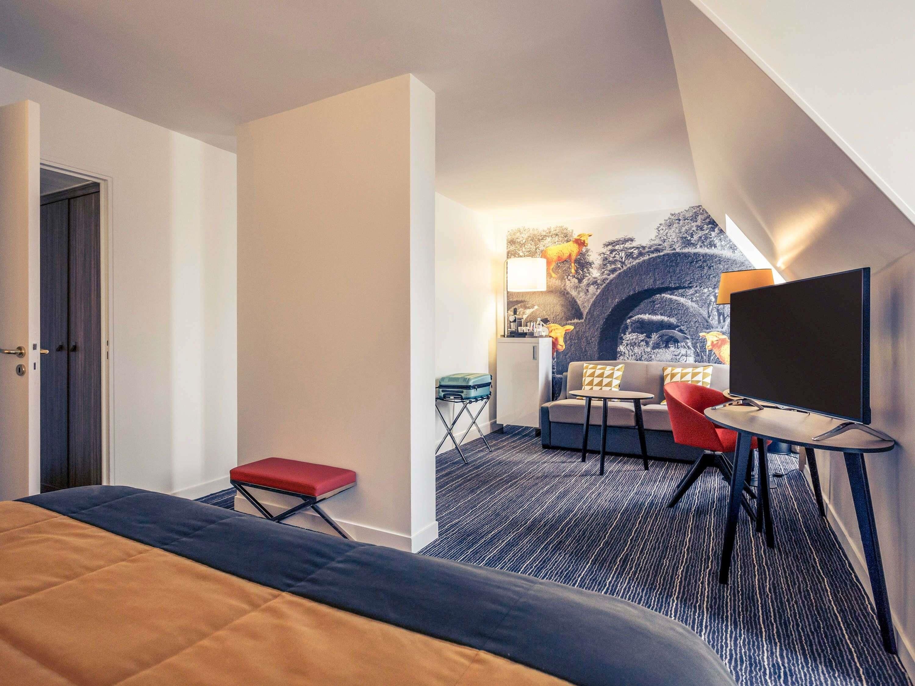 Una habitación de hotel con cama, escritorio, silla, sofá y televisor.