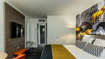 A hotel room with a bed, a TV, a desk, and a chair.