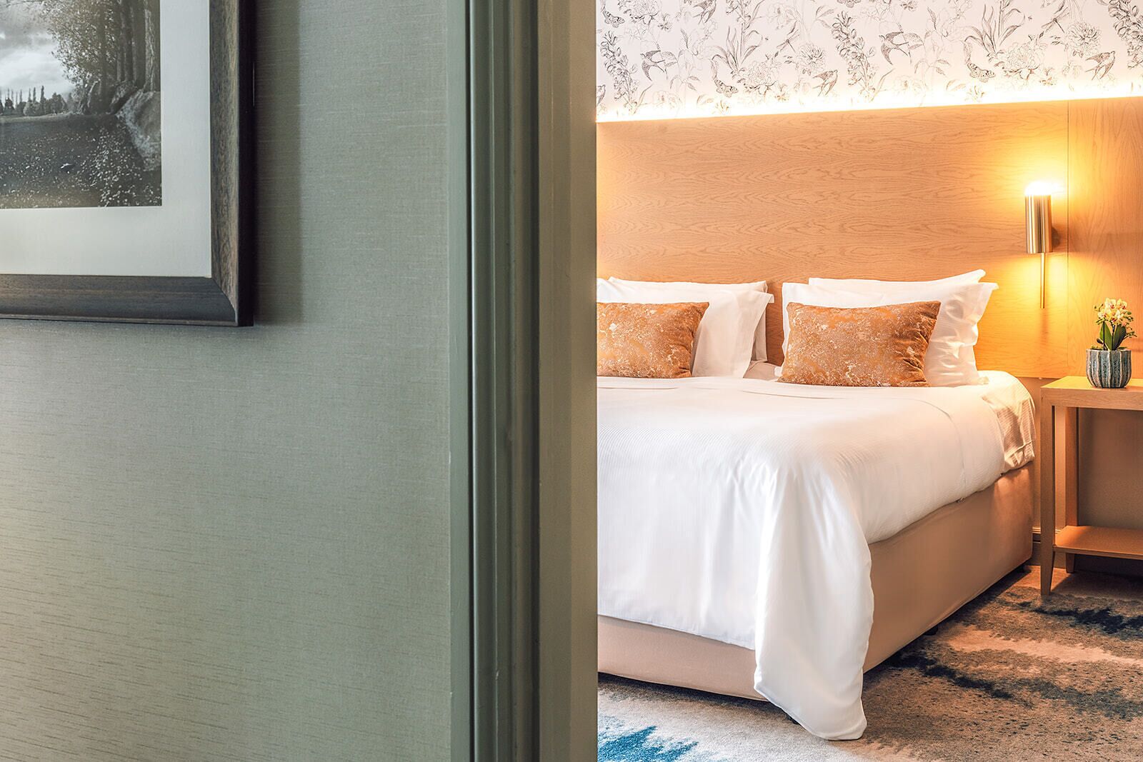 A hotel room with a bed, pillows, a nightstand, a lamp, and a framed picture on the wall.
