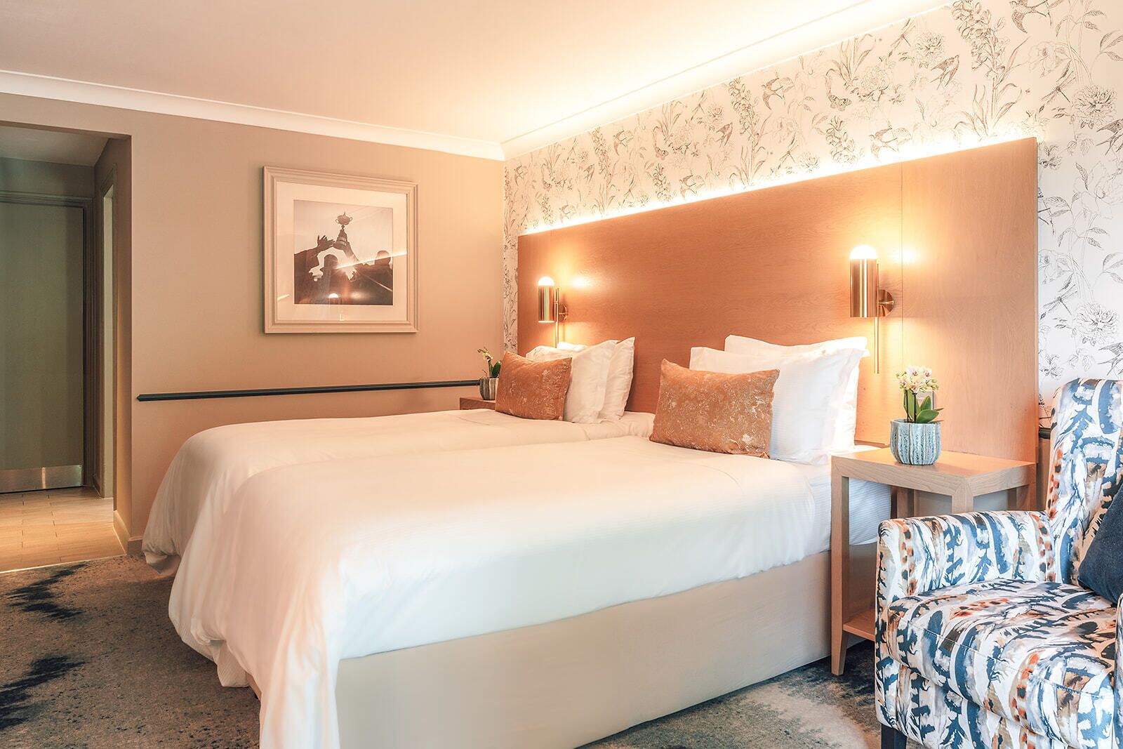A hotel room with a large bed, two bedside lamps, a framed picture on the wall, and a patterned chair.